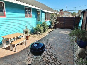 Un jardin avec un barbecue, un banc en bois et des plantes en pot.