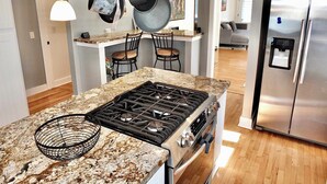 Cocina moderna con encimeras de granito, electrodomésticos de acero inoxidable y ollas colgantes.