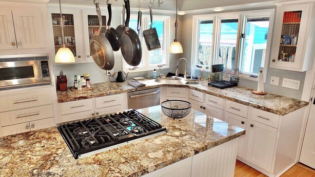 Una cocina moderna con encimeras de granito, armarios blancos, una estufa de acero inoxidable y ollas colgantes.