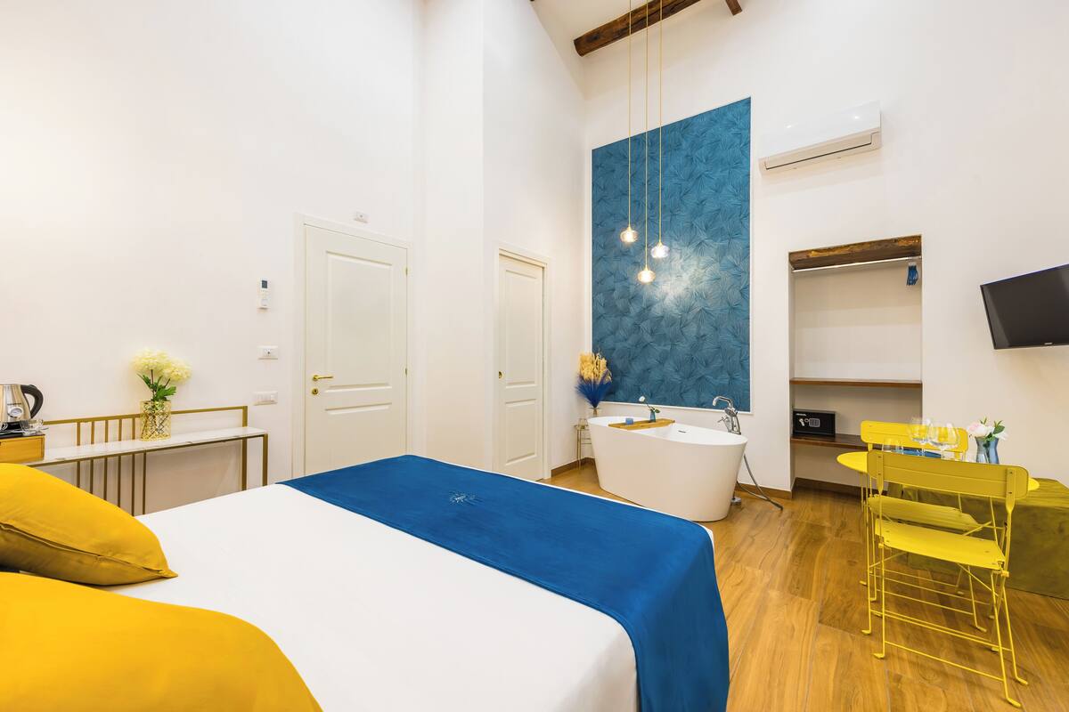 A modern hotel room with a bed, a large mirror, a bathtub, a desk, and a TV.