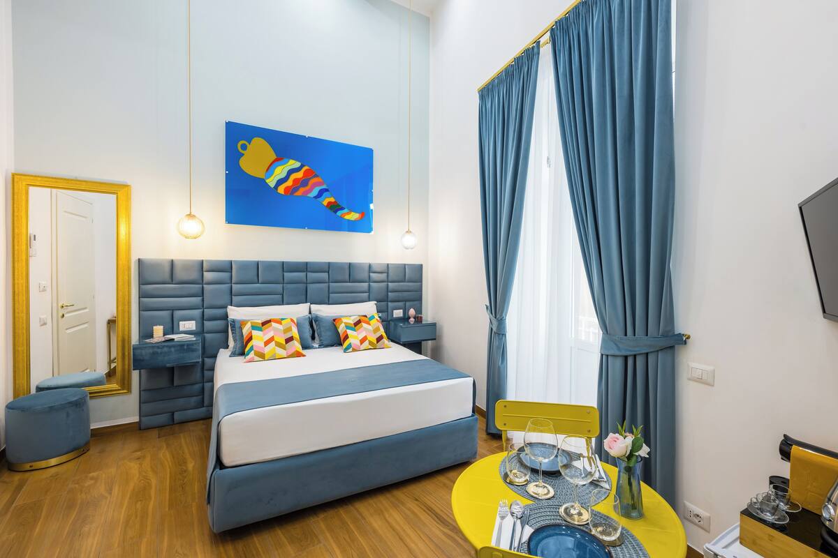A modern bedroom with a large bed, a bedside table, a nightstand, a mirror, and a window with curtains.