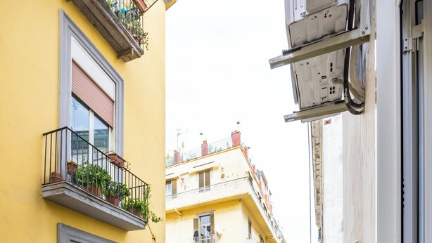 A yellow balcony with breakfast items, including croissants, a cake, and a coffee drink, overlooking a narrow street with yellow buildings. - L Angolo do core (Naples)