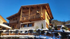 Eine Holzhütte mit Balkon, umgeben von verschneitem Gelände und Bäumen.
