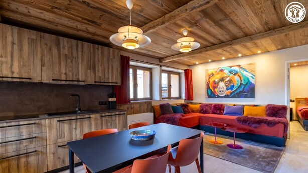 Ein modernes Wohnzimmer mit einem schwarzen Esstisch, orangefarbenen Sesseln und einem farbenfrohen Sofa.