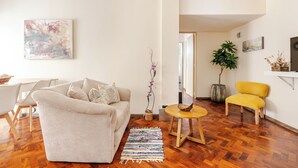 Ein Wohnzimmer mit einer Couch, einem gelben Sessel, einem Holztisch und einer Pflanze.