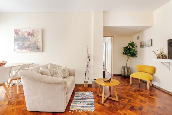Una sala de estar con un sofá, un sillón amarillo, una mesa de centro de madera y una planta.