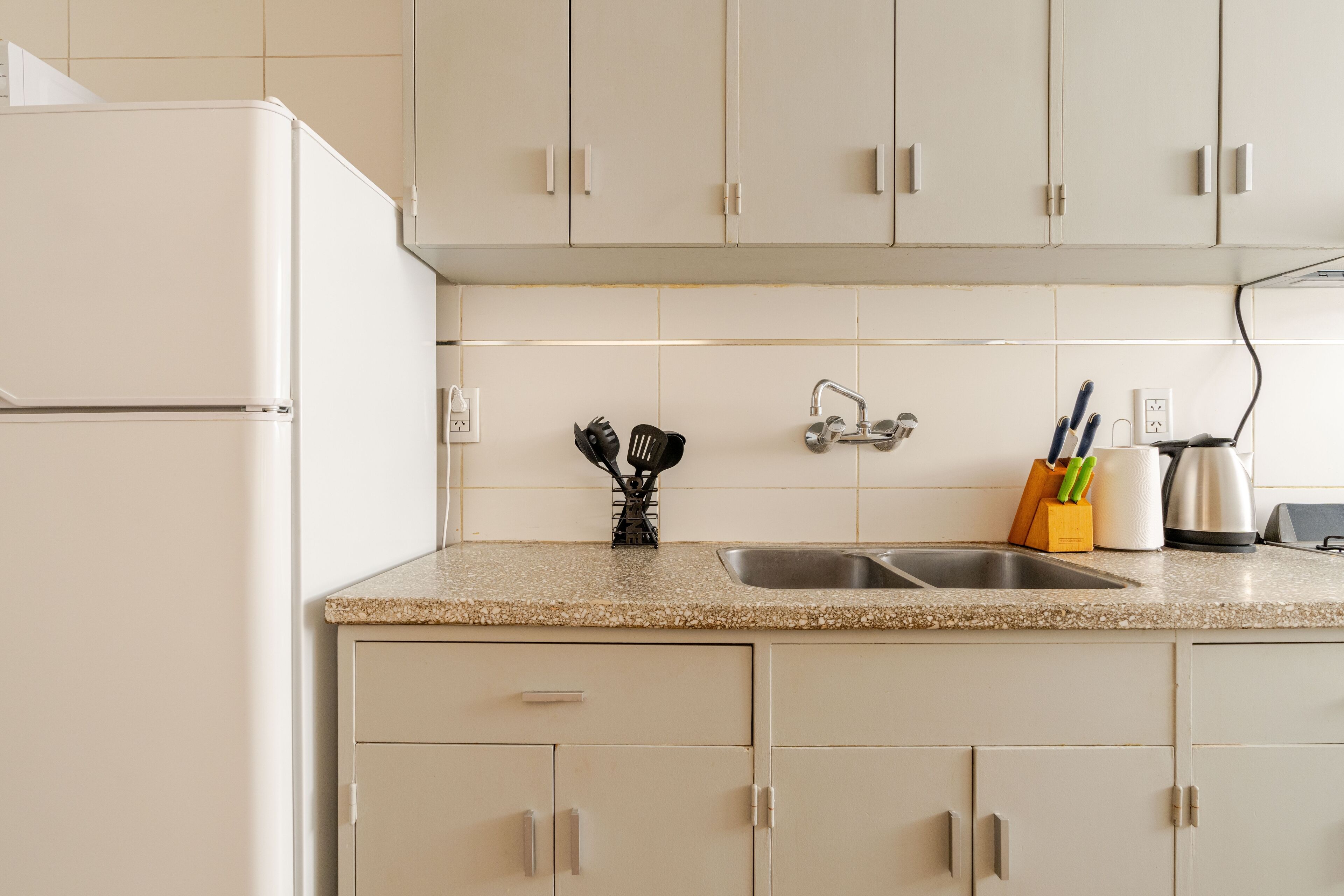 A kitchen with white cabinets, a granite countertop, a stainless steel sink, and a white refrigerator.