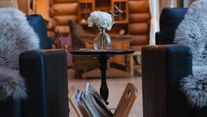 Ein rustikales Blockhaus-Interieur mit Kamin, einem Tisch mit Blumenvase und zwei Fellstühlen.