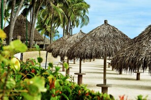 Una playa con sombrillas de paja y palmeras.