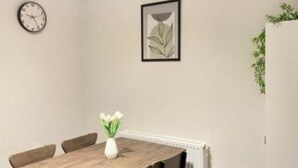 A dining area with a wooden table, four chairs, a vase with flowers, a clock, and a framed artwork on the wall. - Kisobi Home Bedroom 1 (Kingston upon Hull)