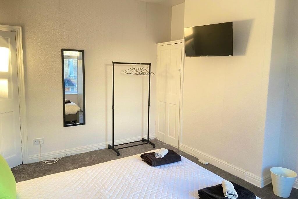 Ett hotellrum med en säng, en spegel, en tv som är monterad på väggen och en klädstång.
