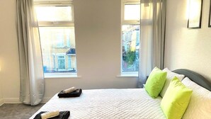 A hotel room with a bed, two windows, and a view of buildings outside. - Kisobi Home Bedroom 1 (Kingston upon Hull)