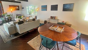 A cozy living room with a round wooden dining table, blue chairs, and a sofa. There are potted plants, books, and a lamp on the table. - Cozy, private & charming 3bd/2ba cottage in a magical little village by the Sea (Newport Beach)