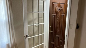 Une pièce dotée d’un plancher en bois, d’une porte blanche avec des panneaux de verre et d’une porte en bois ornée de sculptures complexes.