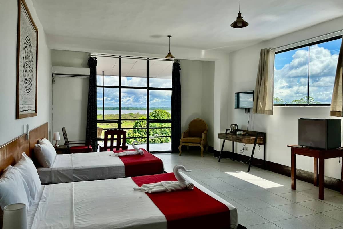 Habitación de hotel con dos camas, un escritorio, una silla, un televisor y un ventanal con vistas al exterior.