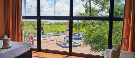 A hotel room with a large window offering a view of a landscaped area with a pool and greenery.