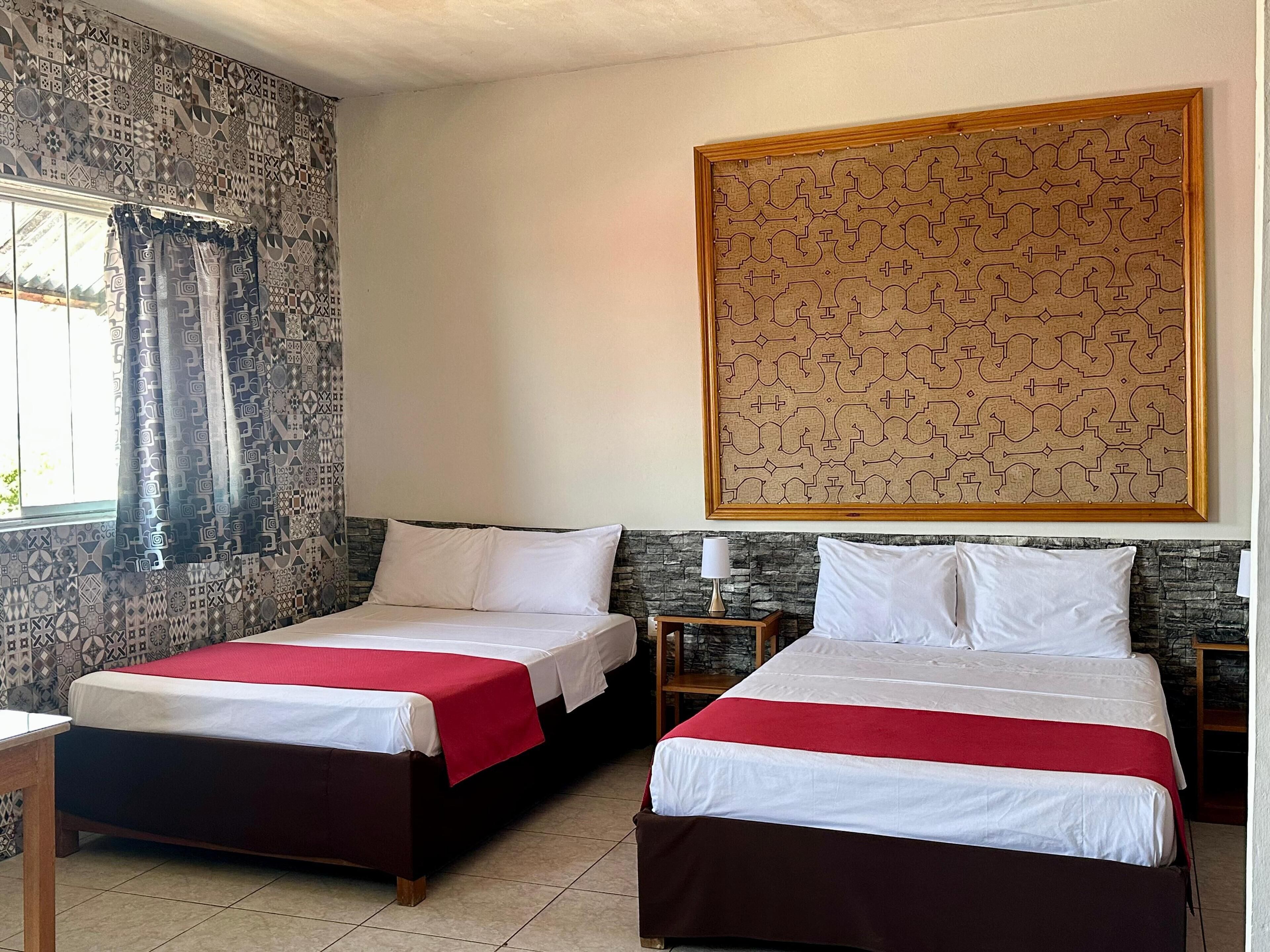Een hotelkamer met twee bedden, een muur met een steenmotief, een gordijn met patroon en een lijstwerk met kunst.
