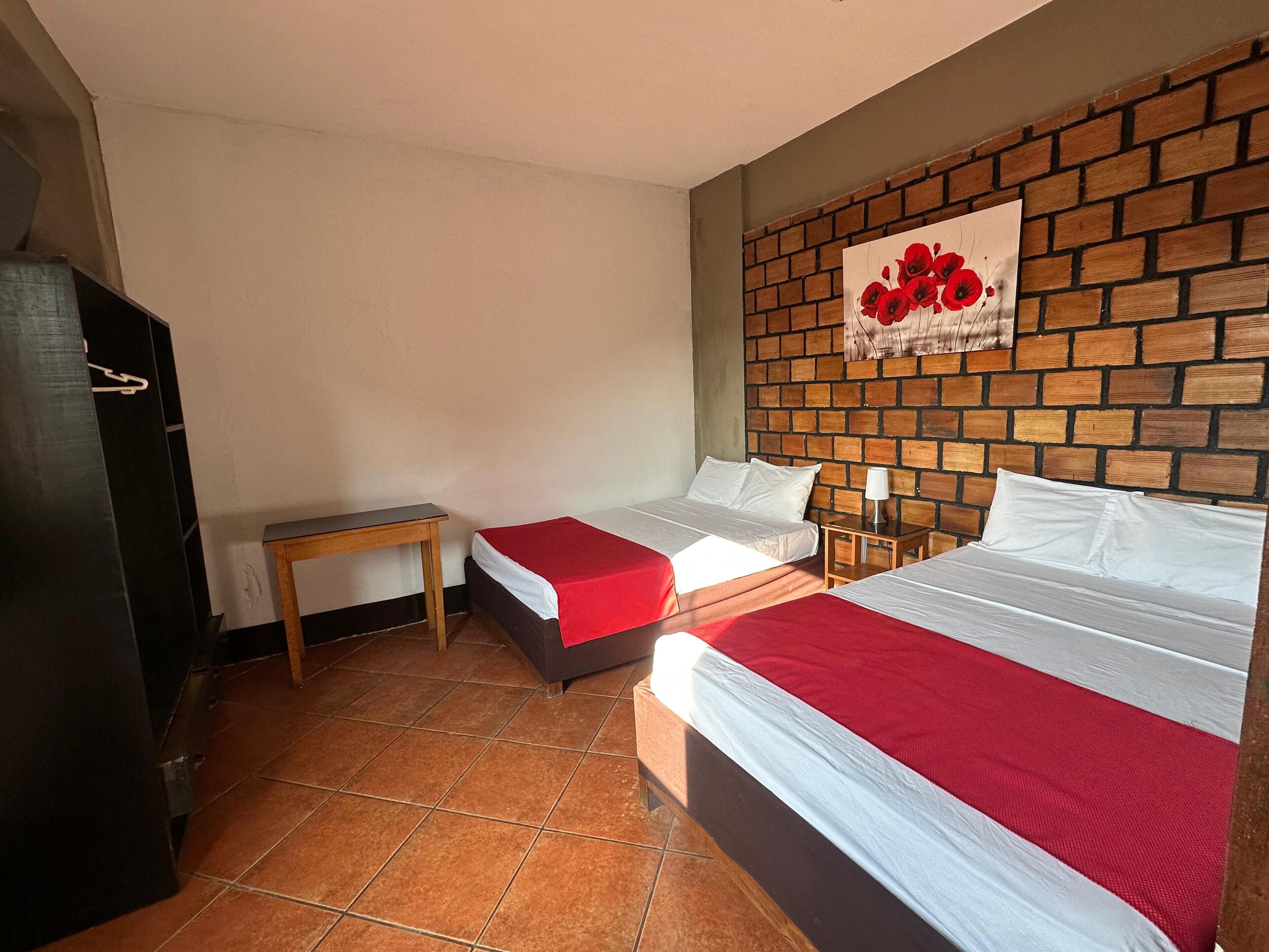 A hotel room with two beds, a brick-patterned wall, a small table, and a wall-mounted artwork.