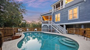 A backyard with a swimming pool, wooden deck, and a two-story house with a balcony.
