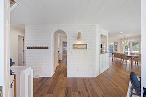 Una cocina amplia con paredes de ladrillo blanco, piso de madera y un comedor con sillas y una mesa.