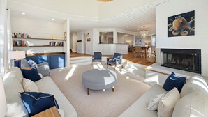 A modern living room with a fireplace, a round ottoman, and a bookshelf.