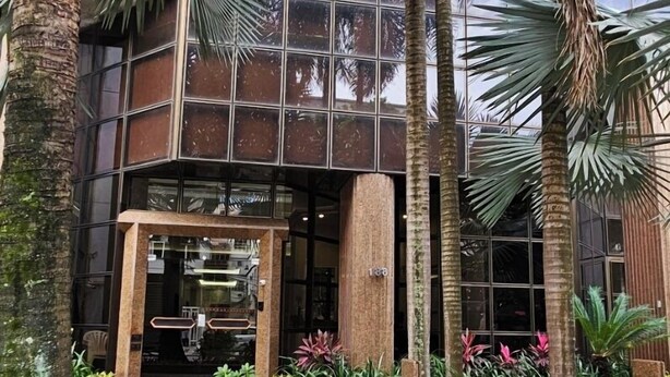 A modern building with a glass facade, surrounded by lush greenery and palm trees. - Sua Casa no Rio Ipanema 2Qts com Garagem (Rio de Janeiro)