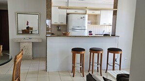 A compact kitchen with a refrigerator, a dining table with chairs, and a bar stool area. - Sua Casa no Rio Ipanema 2Qts com Garagem (Rio de Janeiro)