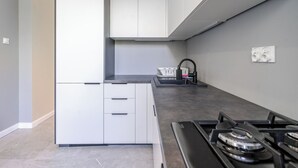 Une cuisine moderne avec des meubles blancs, un plan de travail noir, une cuisinière à gaz et un évier avec un robinet.
