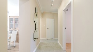 Un couloir avec une porte blanche, une œuvre d’art abstraite accrochée au mur, et un coin repas avec des chaises et une table blanches.