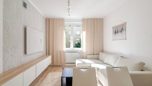 Un salon moderne avec un canapé, une table basse, un téléviseur fixé au mur et une fenêtre avec des rideaux.