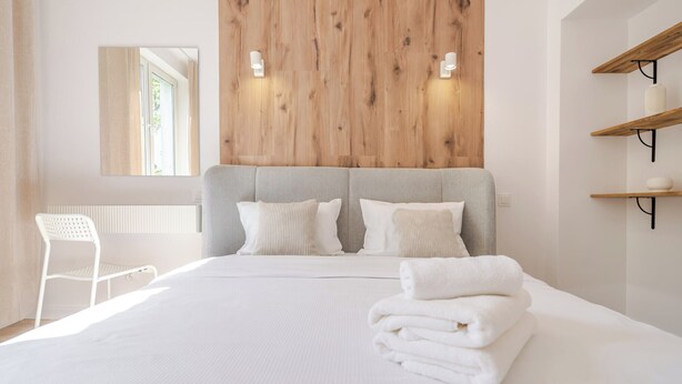 Une chambre à coucher comprenant un lit, deux tables de chevet, une chaise, un mur décoratif en bois et un miroir.