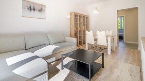 Un salon moderne comprenant un canapé, une table basse, un coin repas avec des chaises, un meuble et un tableau accroché au mur.