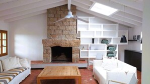 Una sala de estar con chimenea de piedra, muebles blancos y un ventilador de techo.