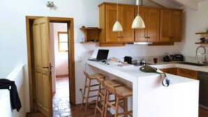 Una cocina con armarios de madera, encimera blanca, dos taburetes de bar, una computadora portátil y una lámpara colgante.