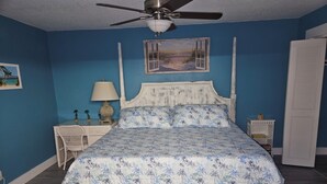 A bedroom with a bed, a ceiling fan, a nightstand, a lamp, and a door. - St. Lucie Breezes 2 (Palm City)