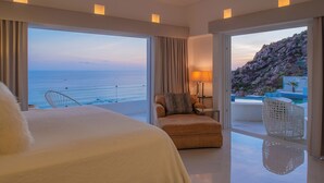 Een hotelkamer met een groot bed, een stoel, een tafel en uitzicht op zee en een zwembad.