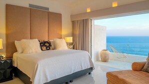 Een moderne hotelkamer met een groot bed, een balkon met uitzicht op zee en een zithoek met een stoel en een vaas.