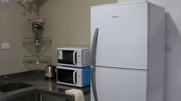 A kitchen with a white refrigerator, a microwave, and a water heater on the wall.