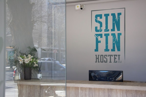 Una recepción con un cartel que dice "SIN FIN HOSTEL" y una planta en maceta al lado.