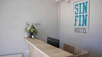A reception desk with a wooden top, a potted plant, and a sign that reads "SIN FIN HOSTEL".