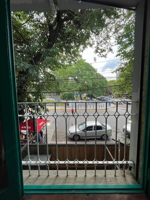 Vista desde un balcón con barandilla de metal, con vista a una calle con coches y árboles.