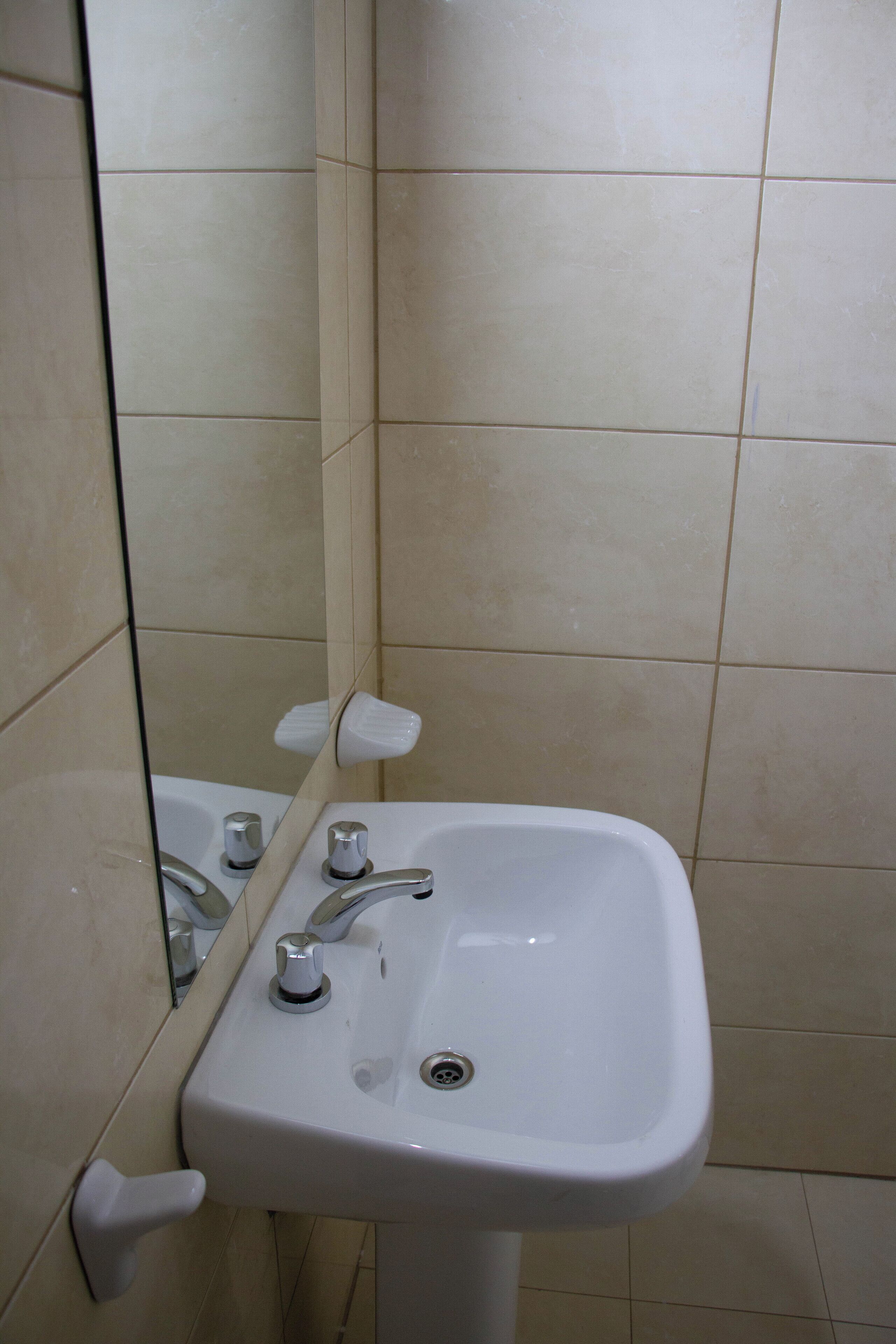 A bathroom with a white sink, two faucets, and a mirror.