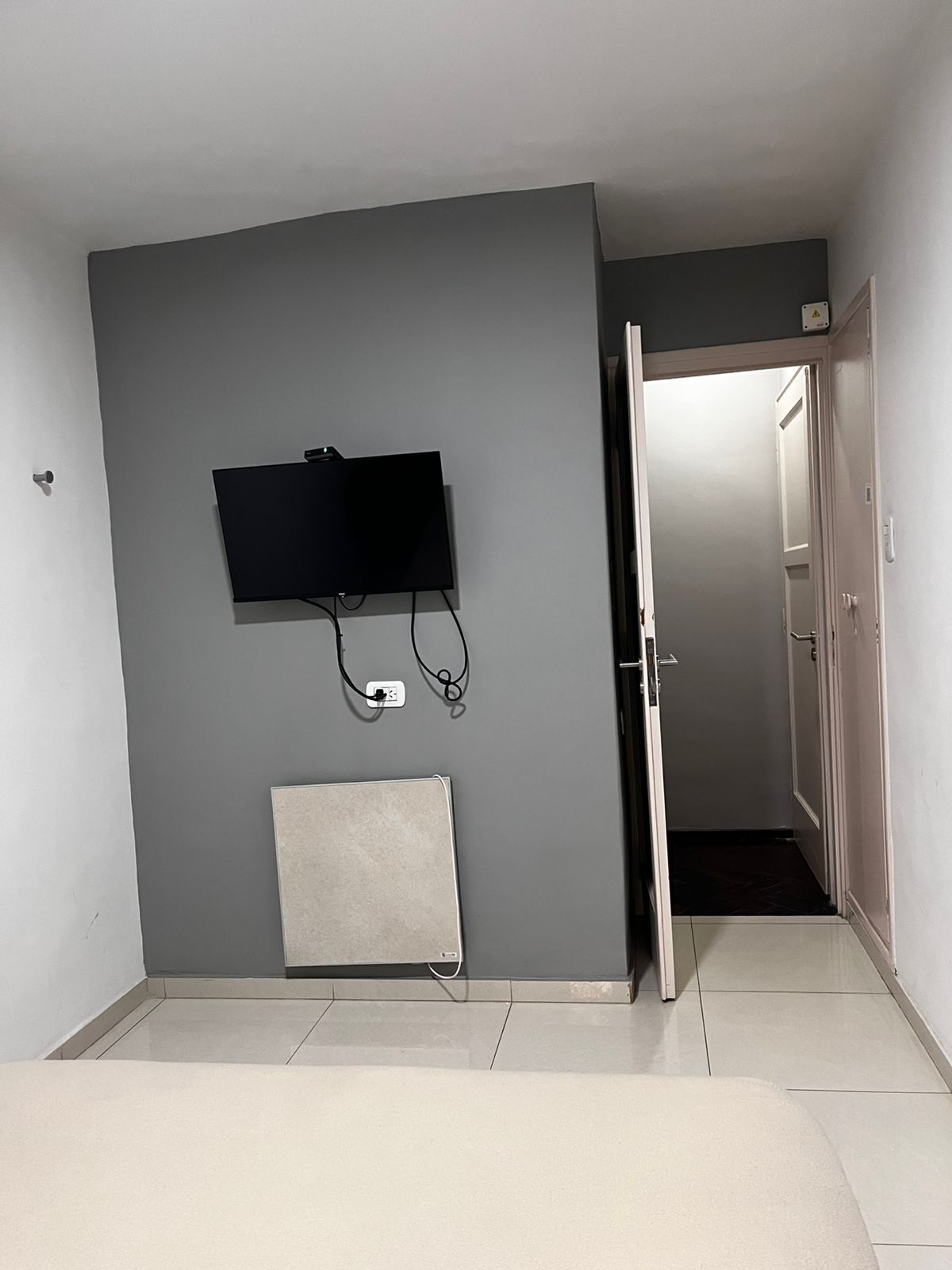 A room with a flat-screen TV mounted on the wall, a power outlet, and a door leading to another room.