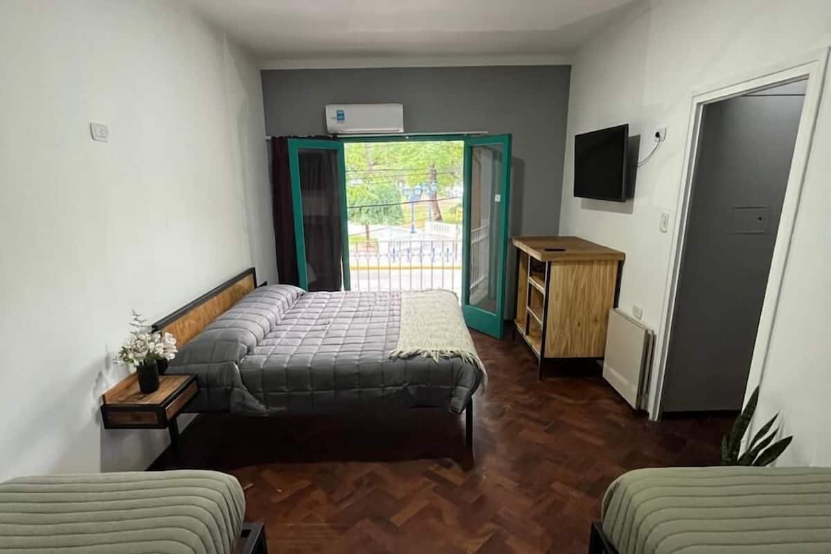 A room with two beds, a small table, a TV, and a sliding door leading to an outdoor area.