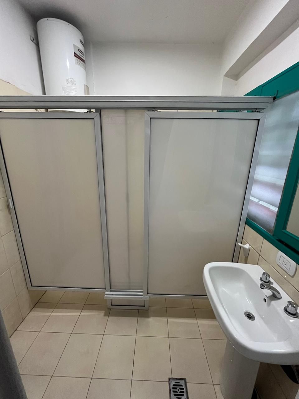 A bathroom with a white sink, a mirror, and a toilet. There is a ventilation unit above the toilet and a vent on the wall.