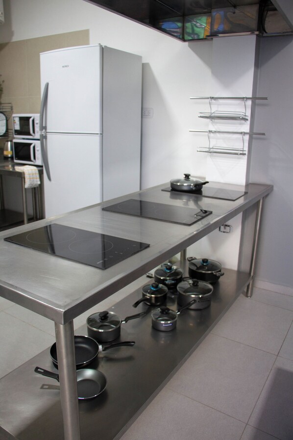 A modern kitchen with a stainless steel countertop, a built-in oven, and a refrigerator. - Sin Fin Hostel (Mendoza)