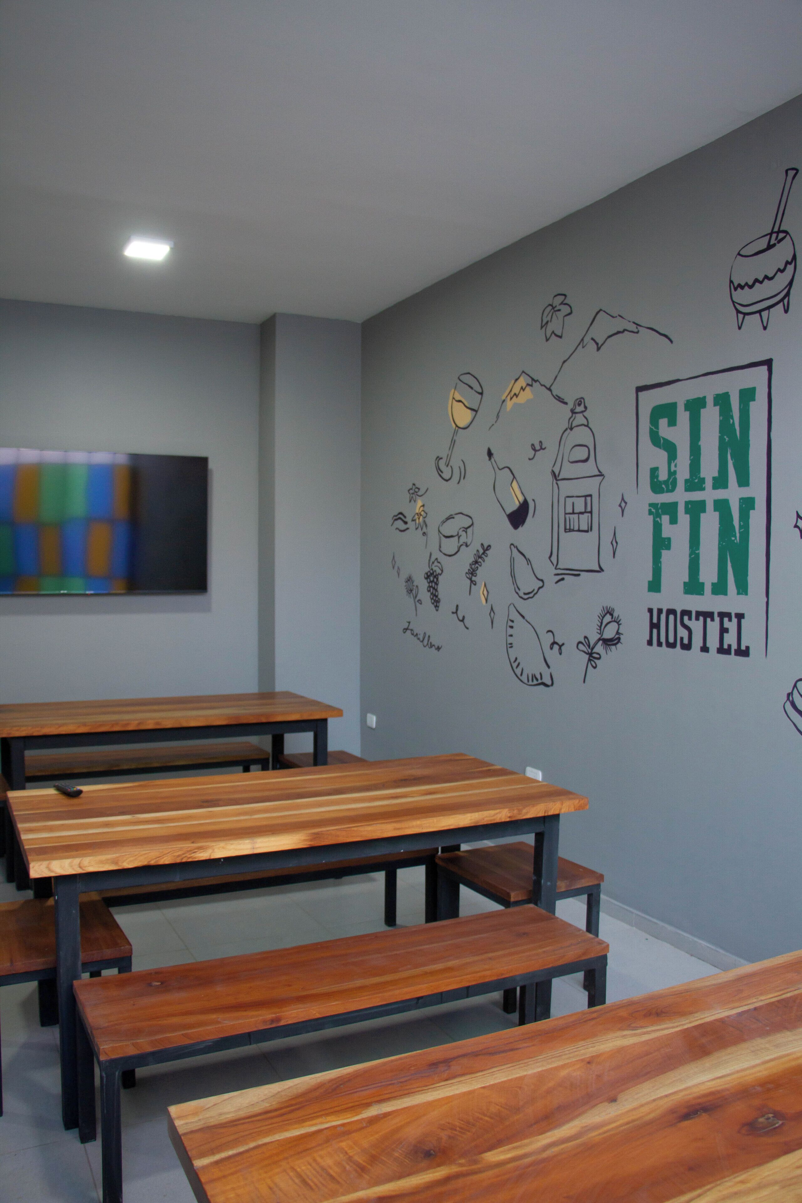 A hostel room with wooden benches, a flat-screen TV, and a wall decorated with doodles and the text "SIN FIN HOSTEL".