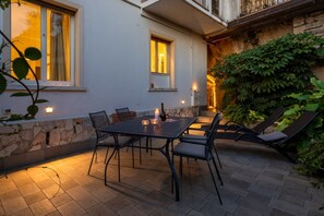 Una terrazza esterna con tavolo e sedie, un muro in pietra e vista su un edificio con finestre.