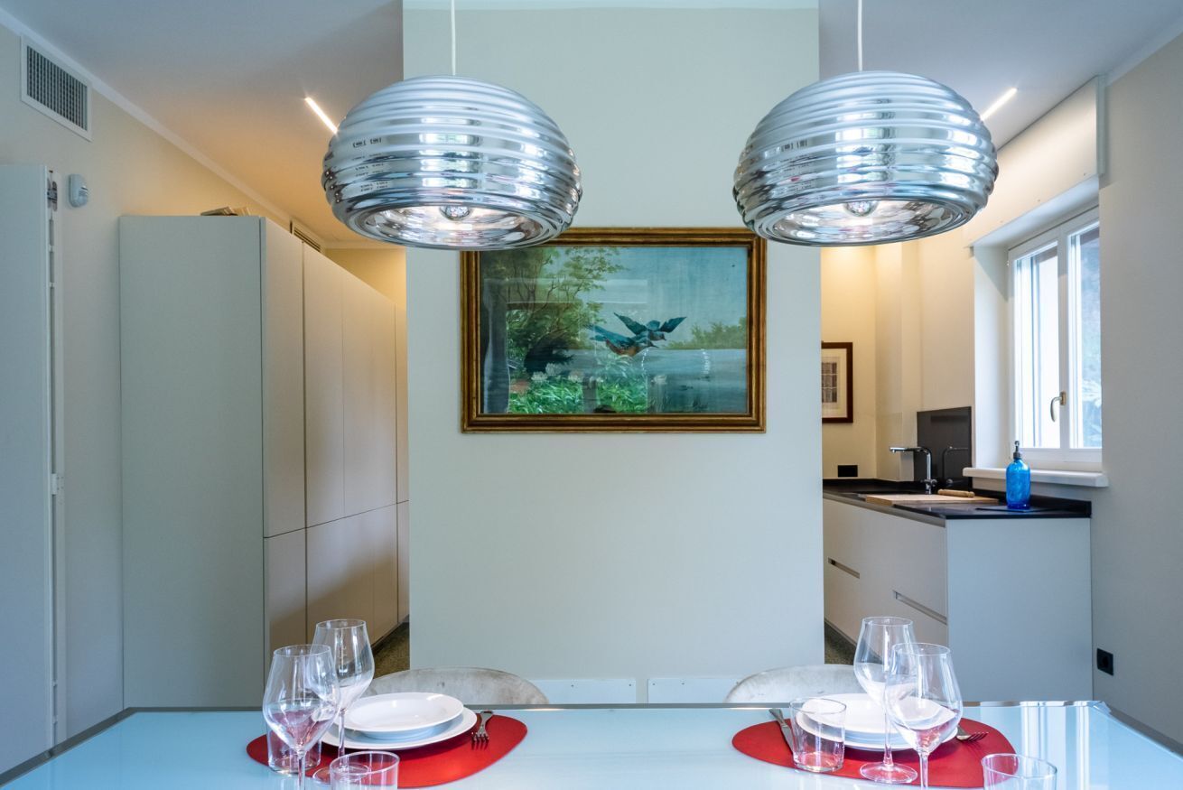 Un coin repas avec une table blanche dressée pour deux personnes, deux lampes suspendues et un tableau encadré accroché au mur.