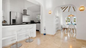A modern kitchen with white cabinetry, stainless steel appliances, and a bar area with white stools. - Casa Blanca | private pool - garden - bbq (Estepona)
